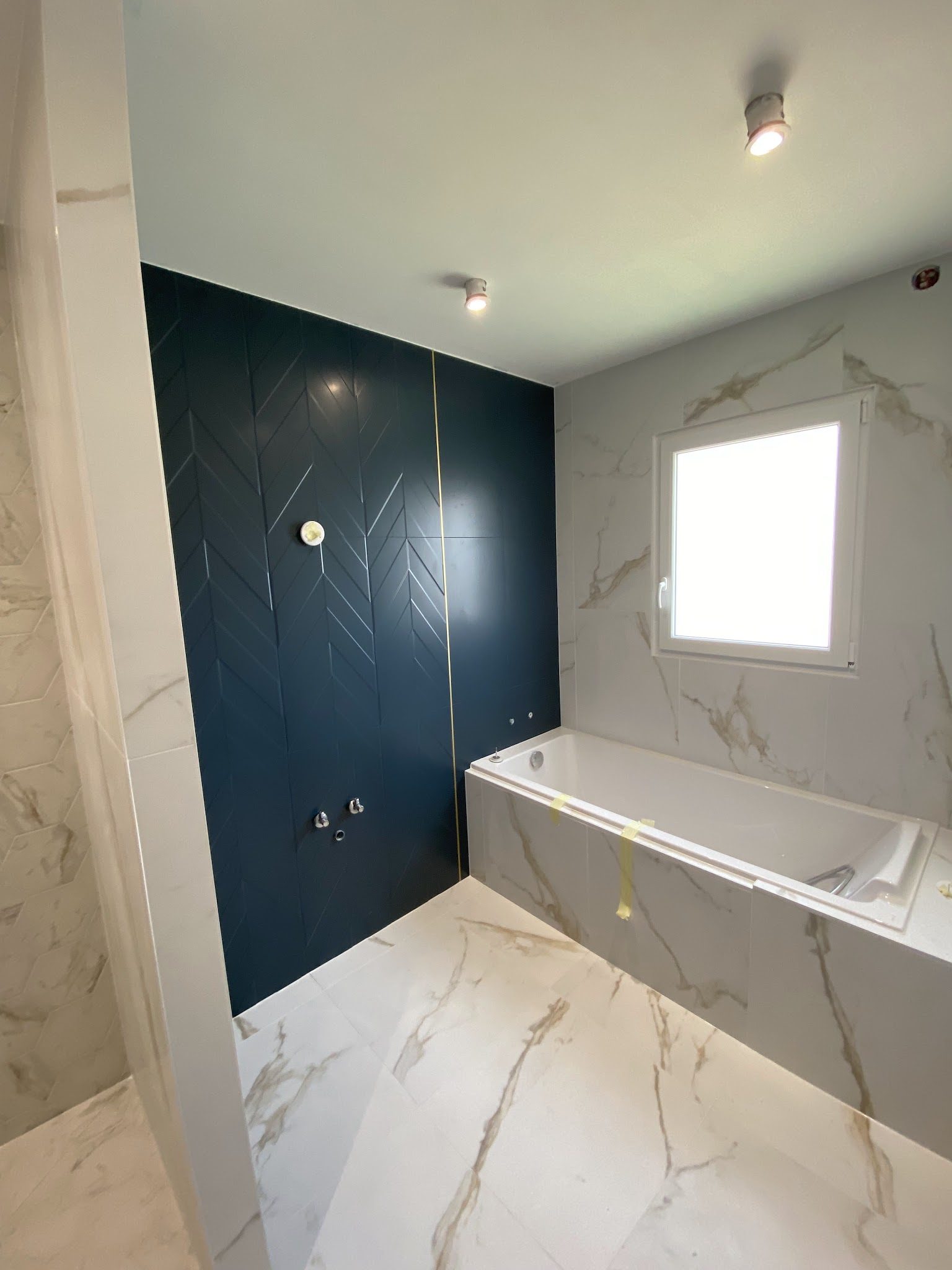 Salle de bains : sol effet marbre, mur bleu nuit en chevrons, baignoire habillée